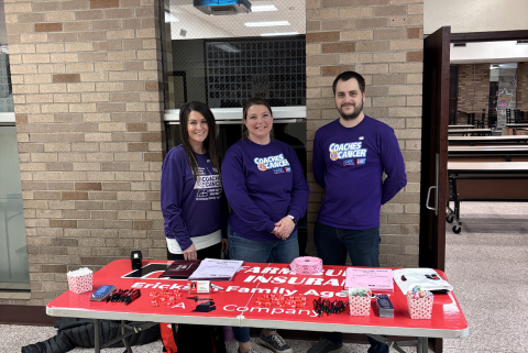 Team standing in front of a table at coaches vs cancer